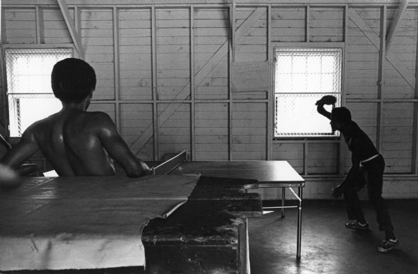 Two people playing table tennis with one man watching. Photograph is part of a group of images taken of Cuban refugees who had arrived as a result of the Port of Mariel exodus, and were housed at Camp McCoy, Wisconsin.