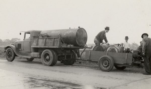 Men pumping DDT from a tank on the back of a truck to be sprayed into a field.