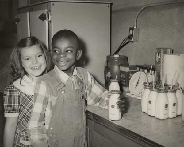 A young boy and girl pose together as they take their bottles of milk at school.