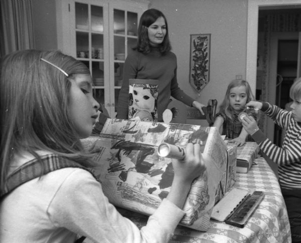 Elizabeth and Katherine Davey and Curtis Liposcak use their creative talents to wrap Christmas gifts under the supervision of Peggy Davey, a member of Women for a Peaceful Christmas.