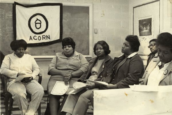 Five women are seated with an ACORN banner over the blackboard behind them. A man is seated behind them on the right.