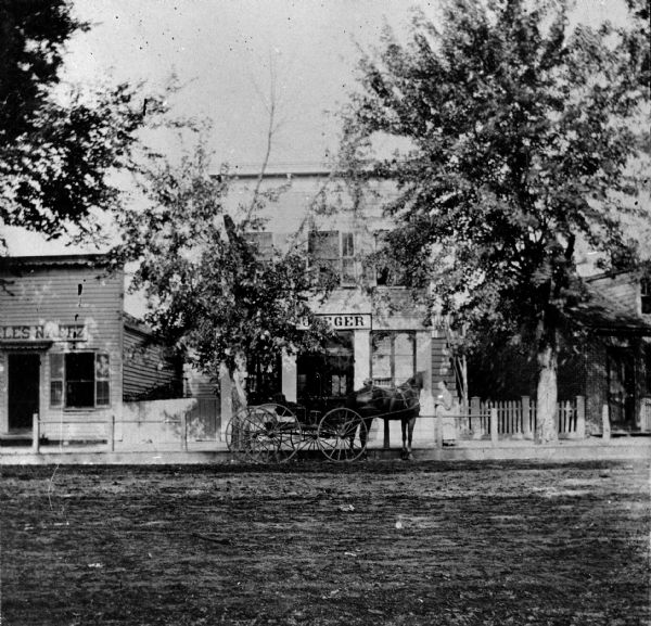 View from across street of two buildings on Water Street during the 19th century. The building on the right was built in 1866 by Christian Schumm. It later became famous as the old harness shop owned by Hugo Schwenker where Wisconsin writer August Derleth spent much of his time. On the left is the Naggz Building which was built in 1869.