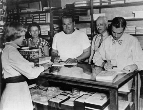 Wisconsin writer August Derleth (center) autographing copies of his book, <i>Sac Prairie People</i>. The other individuals in the photograph are not known. <i>Sac Prairie People</i>, which was published in 1948, was part of many literary works Derleth wrote concerning his home town of Sauk City.