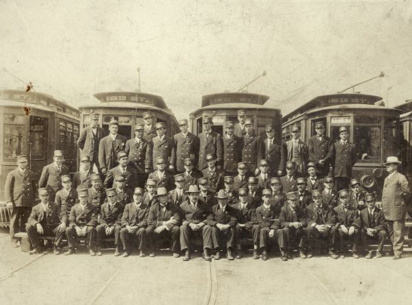 Milwaukee streetcar conductors posed in front of streetcars. Edwin Salber shown second row fifth person from the left.