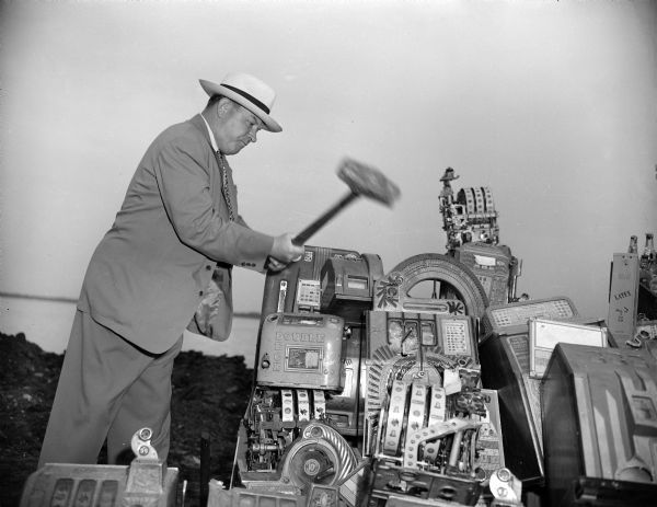 John Roach, director of the state beverage and cigarette tax division, using a sledge hammer to smash illegal slot machines.