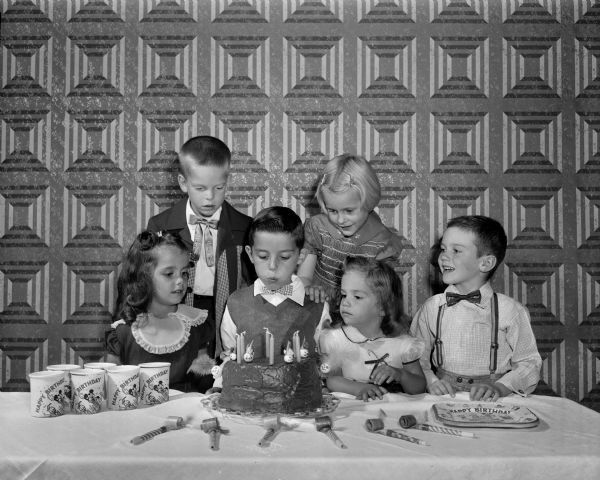 Steven Presenza blowing out the candles on the cake at his sixth birthday party. Included are his two sisters, Lorna Presenza and Paula Presenza, as well as Larry Bakke, Lloyd Sinclair, and Anne Hendrickson.