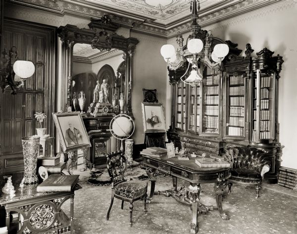 Interior view of a room in the Bradley house, including paintings, a globe, fine furniture, a bookcase, and a large, ornate mirror over the fireplace.