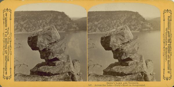 Stereograph of a rock formation known as Turk's Head high above Devil's Lake. Bluffs are on the far shoreline.