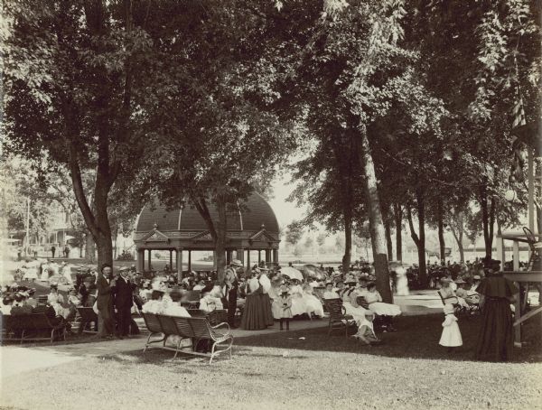 A large group of well-dressed people are gathered around a gazebo at Besthesda Springs.