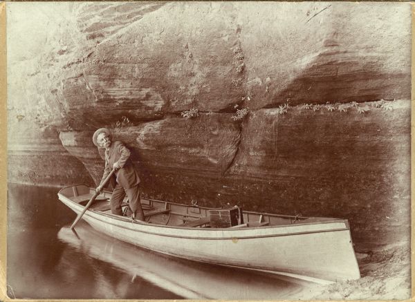 Henry Hamilton Bennett poling his boat close along a rock formation in the Wisconsin Dells.