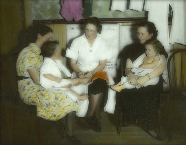 A nurse sits between two mothers with babies on their laps. They are discussing "individual problems of maternal and child health."