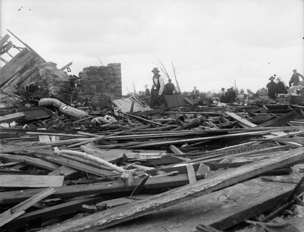A man works to clear debris in the aftermath of a tornado. Other men, women and children are gathered nearby.