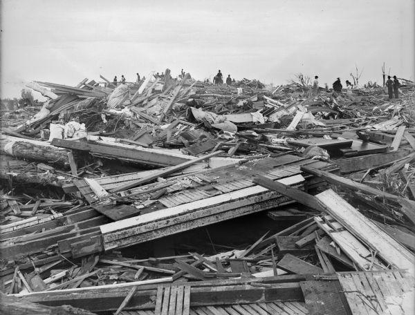 Field of debris left in the wake of a tornado. A crowd of people are observing the destruction from a high vantage point.