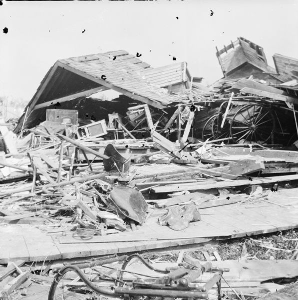Debris left after tornado. A portion of a roof from a collapsed building lies on top of the debris, including the wheels of a carriage or cart.