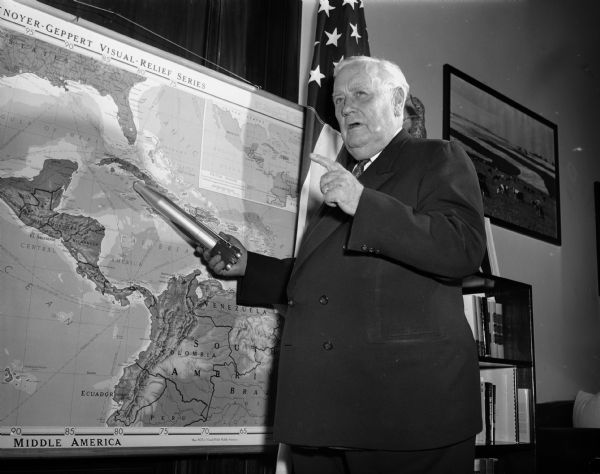 Senator Alexander Wiley posing with a model of a missile pointed at a map of Cuba.