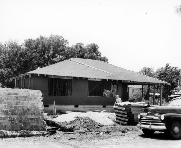Exterior view of front of the house of Daisy and L.C. Bates. The house is under construction. The walls and roof have been built, and a pile of bricks are on the left.