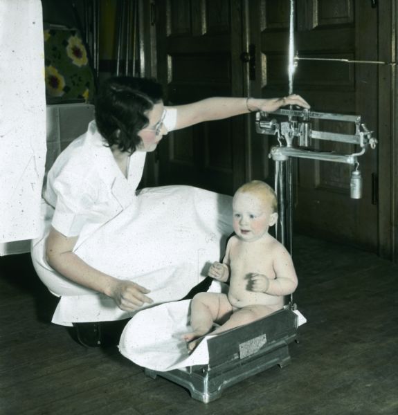 A nurse weighing a baby in a scale on the floor.
