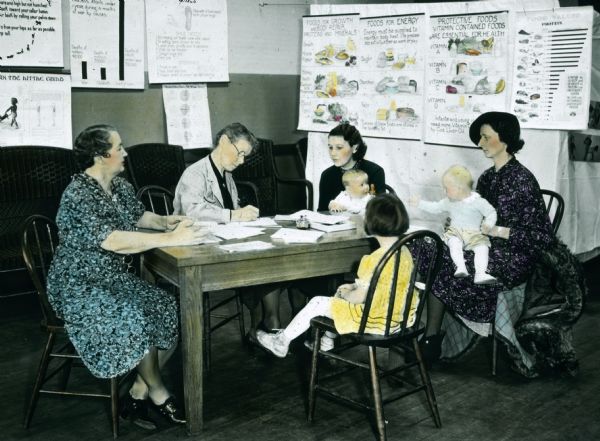 Women, who are accompanied by their children, register at the Health Center. On the walls are displayed posters on health and food.