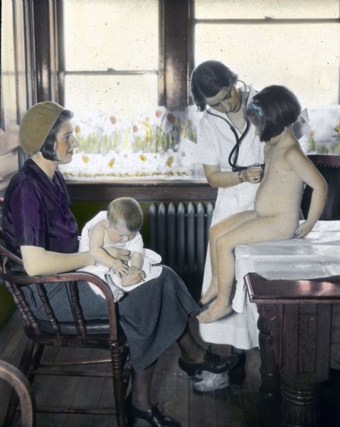A nurse or doctor at the Health Center gives a girl a physical examination as the mother, who is holding a baby, looks on.