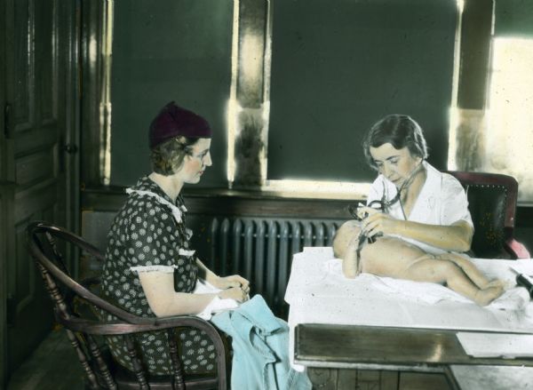 A nurse or doctor gives an infant a physical examination at the Health Center as the baby's mother looks on.