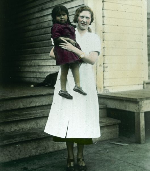A nurse poses outdoors holding a Native American girl at the Lac du Flambeau Indian reservation.