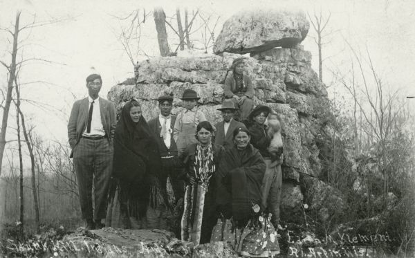 Group of Native Americans-Potowatomi standing in front of rock formation.