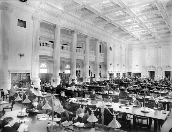 Library Reading Room as completed in 1901, showing skylights and ceiling fixtures, library tables and lights, and many University of Wisconsin students at the tables.