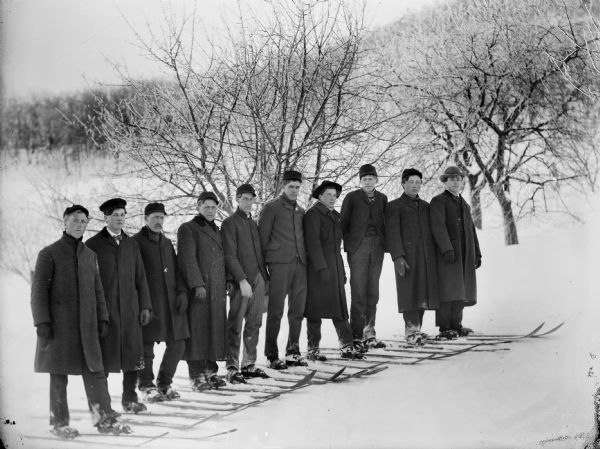 A group of ten men wearing skis posed outdoors in the snow.