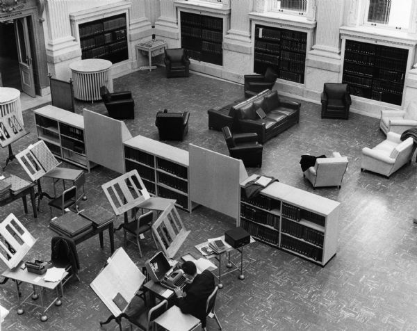 Elevated view from the balcony of the north end of the Wisconsin Historical Society's library reading room showing the recent remodeling. The remodeling divided the large space into smaller functional units, as well as replacing the original furniture and flooring. In the foreground is the area where patrons could read large bound newspaper volumes. Beyond are the chairs purchased for casual reading.