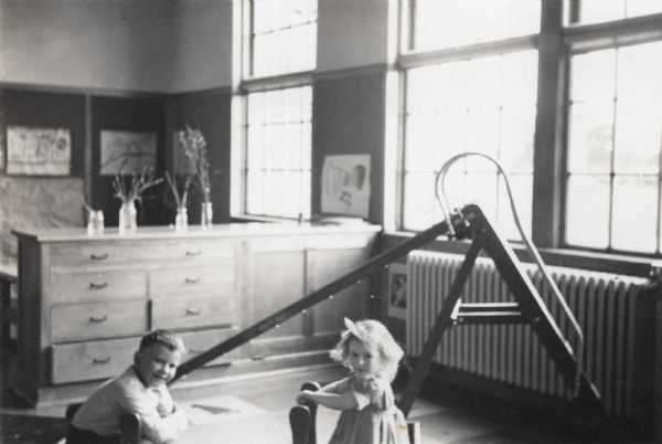 A young boy and a young girl playing in their kindergarten classroom near a ladder and slide.
