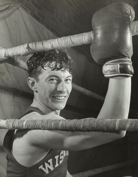 Omar Crocker, a University of Wisconsin-Madison boxer, smiles as he sits in the corner of a boxing ring, wearing his gloves.