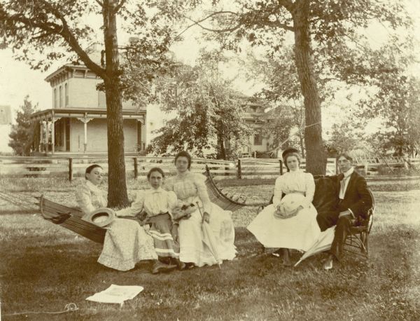 A group portrait of Pearl Clough, Myrtle Stoddard, Fraua Wiswall, Zilla Wiswall, and Roy Stoddard (probably left to right). Three of the women are posed together on a hammock. In the background is a large house.