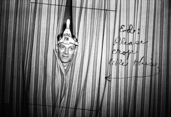 A man with a "King Pin" bowling pin crown on his head peers through curtains at the Lithographers Intercity Bowling Dinner Dance.