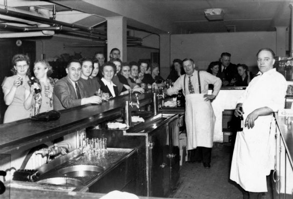 A view from behind the bar in the Lutheran Center Bowling Alley of happy patrons enjoying a beer. One of the two bartenders is also enjoying a beverage.