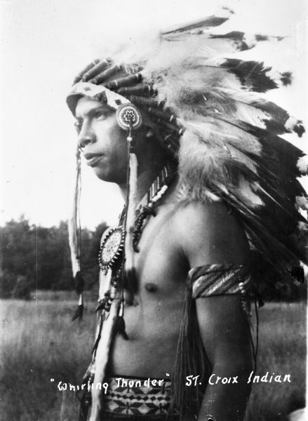 Saint Croix Ojibwa man, bare-chested, wearing a feather war bonnet.