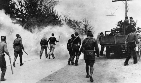 National Guardsmen, who were sworn in as deputies, approach milk strikers through what appears to be a cloud of smoke.