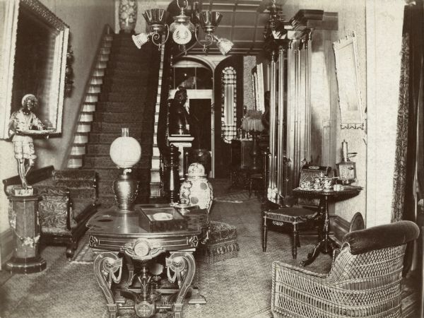 View of the central hall at Villa Louis. The hall is decorated with sculptures, paintings and other decorative items. There is a stairway at left.