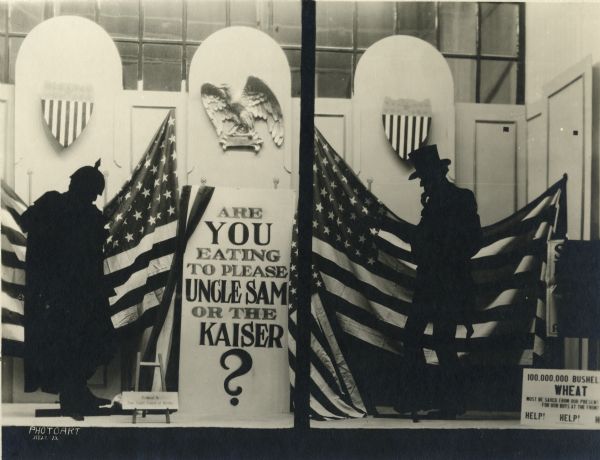 Window display in an unknown storefront featuring American flags, and silhouettes of Uncle Sam and Kaiser Wilhelm II and asking the question "Are you eating to please Uncle Sam or the Kaiser?"