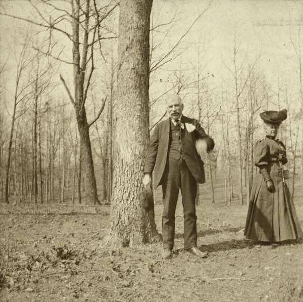 George McMillan poses next to a tree and an unidentified woman. A handwritten caption beneath the image reads, "This tree sheltered me." He was a veteran of the Civil War, 16th Wisconsin Infantry. He survived the Battle of Shiloh by sheltering behind this tree.