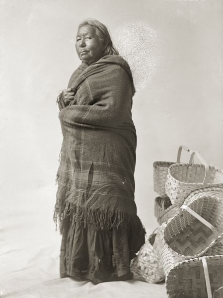 Studio portrait of an elderly Ho-Chunk woman with baskets.