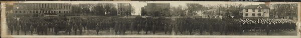 A panoramic photograph featuring the Student Army Training Corp (S.A.T.C) at the University of Wisconsin-Madison standing at attention on Library Mall. In the background is the Wisconsin Historical Society, the Y.M.C.A., the Red Gym, and a portion of both Langdon Street and Lake Street.