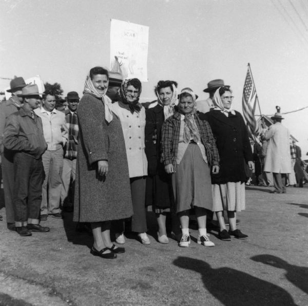 Five striking female workers in headscarves pose together. Men are visible behind them, one of whom carries an American flag.