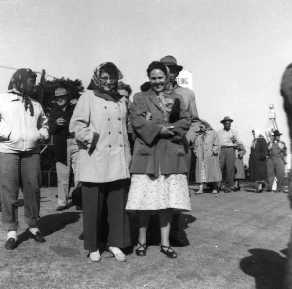 Two female workers on strike pose together, smiling. Other striking workers, both men and women, are visible behind them.