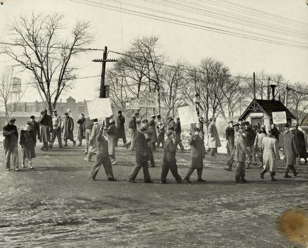 Striking workers near a railroad crossing march in a circle holding handmade signs.