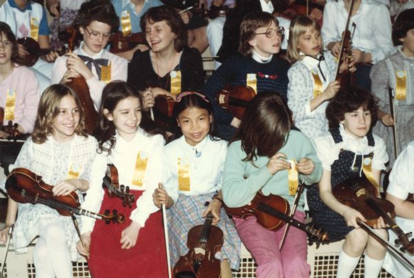 Thuy Nguyen (bottom row, third from left) sits with other girls at a music competition for stringed instruments. She is holding a viola.