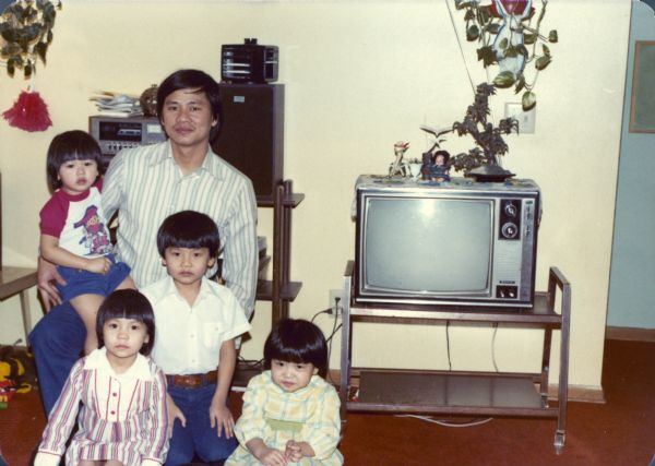 Trong Nguyen poses with his children in the living room, next to the television. Charlie Nguyen sits on his lap. In front of him, from left to right, are Thuy, Minh and Mary Nguyen.