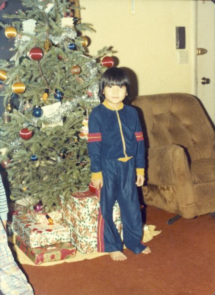 Thuy Nguyen, wearing a track suit, poses in front of a decorated Christmas tree.