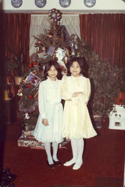 Thuy Nguyen (left) and Mary Nguyen pose in front of a Christmas Tree. They are wearing fancy dresses.