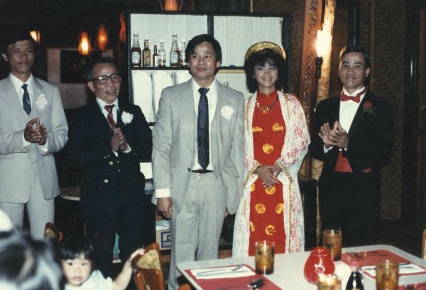 Trong Nguyen, in the center wearing a necktie, poses with the bride and groom, and others at a family wedding. The bride is wearing a traditional Vietnamese wedding dress.