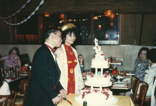A bride and groom, who are relatives of Trong and Hong Nguyen's family, stand with their wedding cake. The bride is wearing a traditional Vietnamese wedding dress.